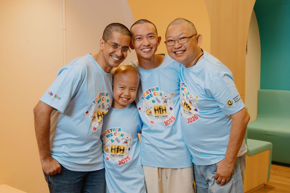 A group wearing matching light blue t-shirts smiles together in an indoor setting.