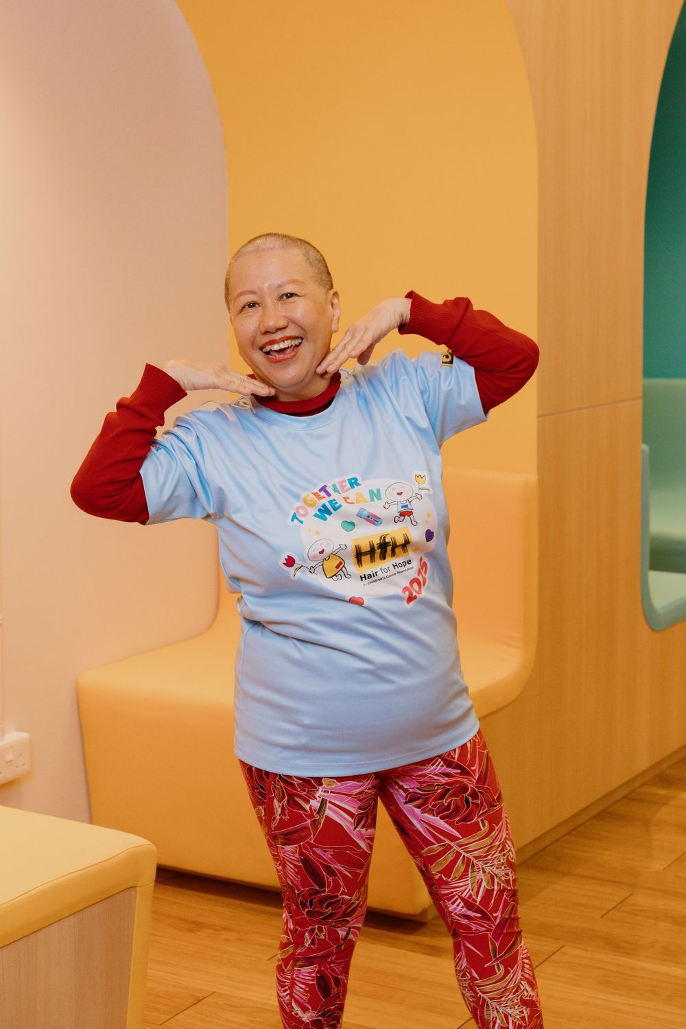 Person in light blue t-shirt with red sleeves and patterned pants poses playfully against yellow wall backdrop.