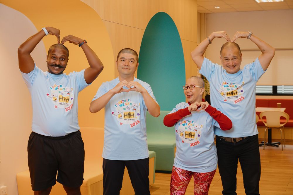 Group wearing matching light blue t-shirts making heart shapes with their hands in an indoor setting.
