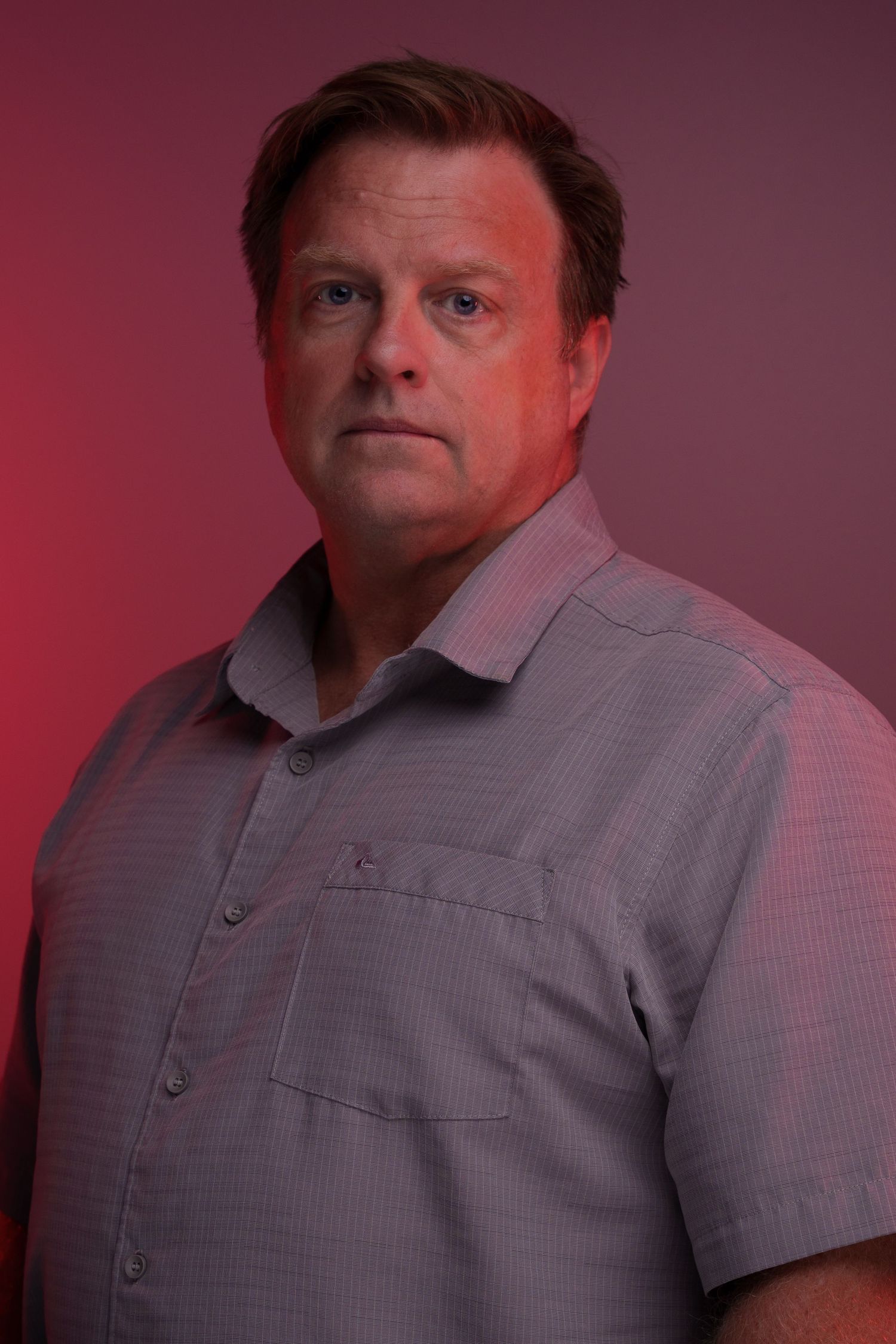 Man in gray polo shirt poses against dark red backdrop, showing various expressions and angles.