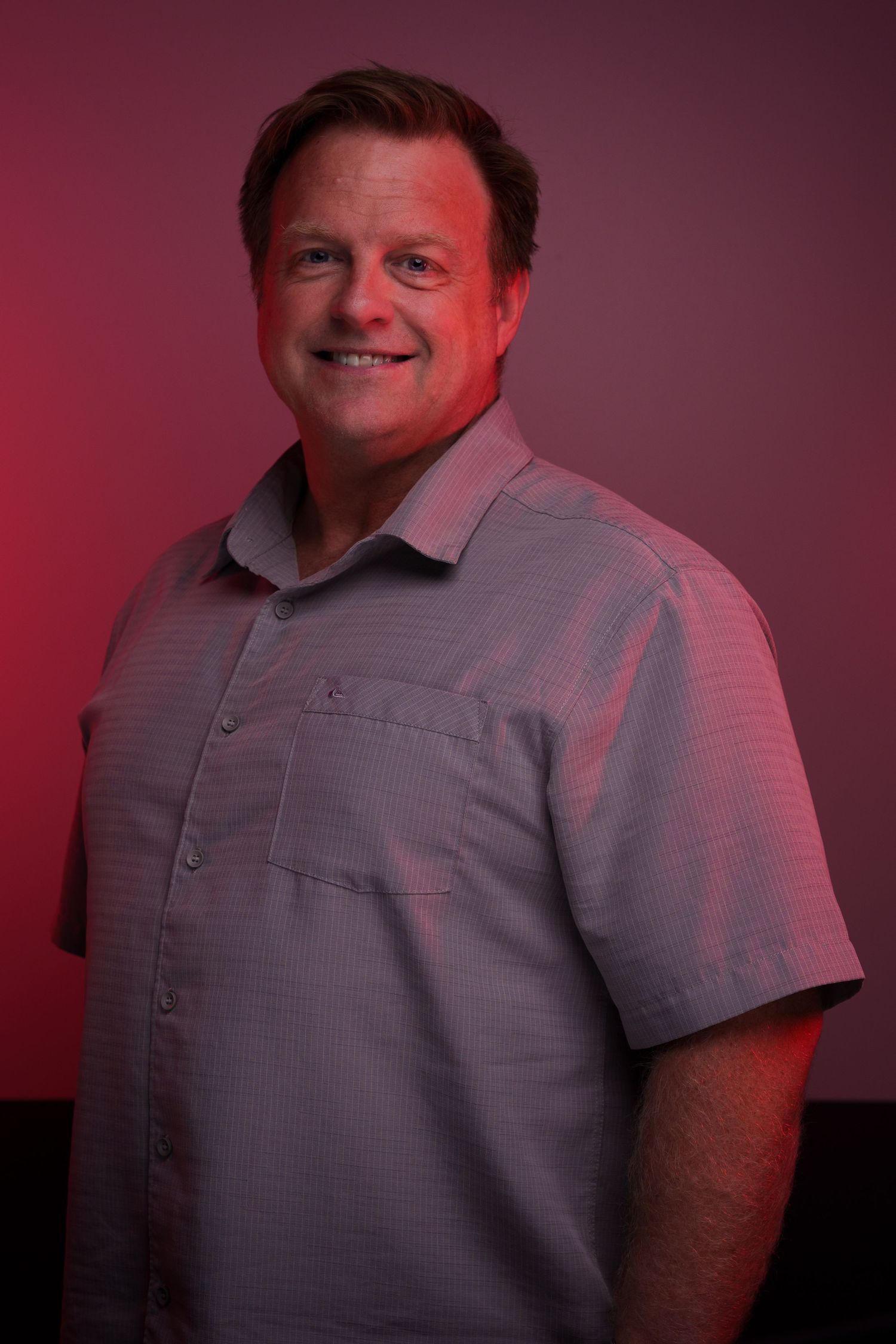 Side profile studio portraits of person in gray polo against maroon background.
