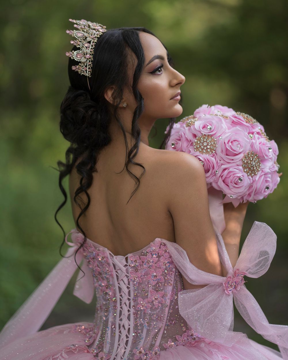 A stunning pink ballgown with ornate beading and ruffles is displayed in a natural outdoor setting.