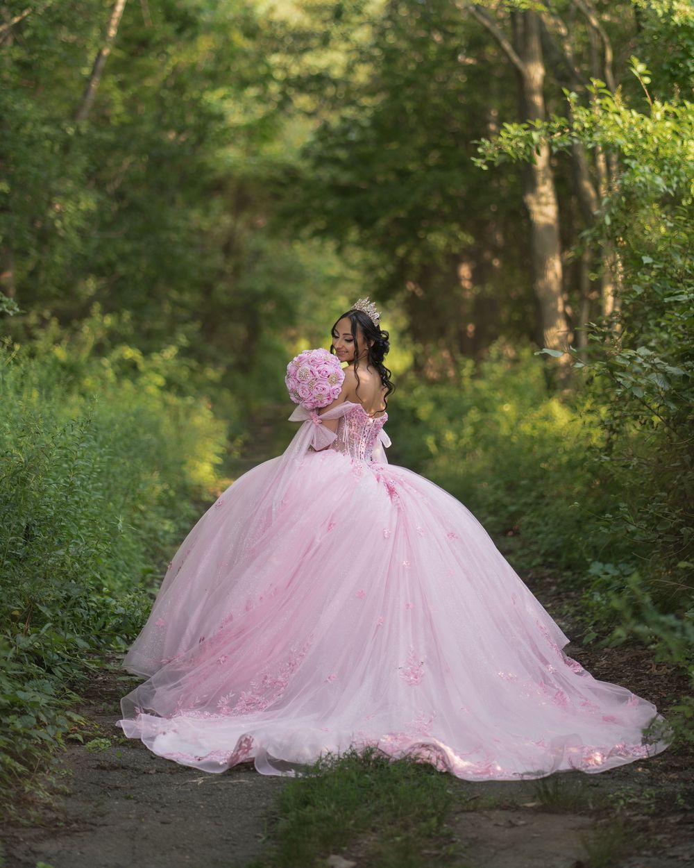 A romantic pink tulle ball gown dress with lace details creates an enchanting scene in a sunlit forest setting.