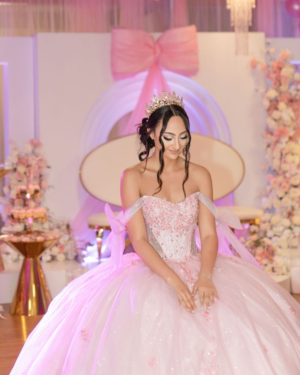 A glamorous quinceanera celebration featuring a pink ballgown in an elegant ballroom with floral decorations.