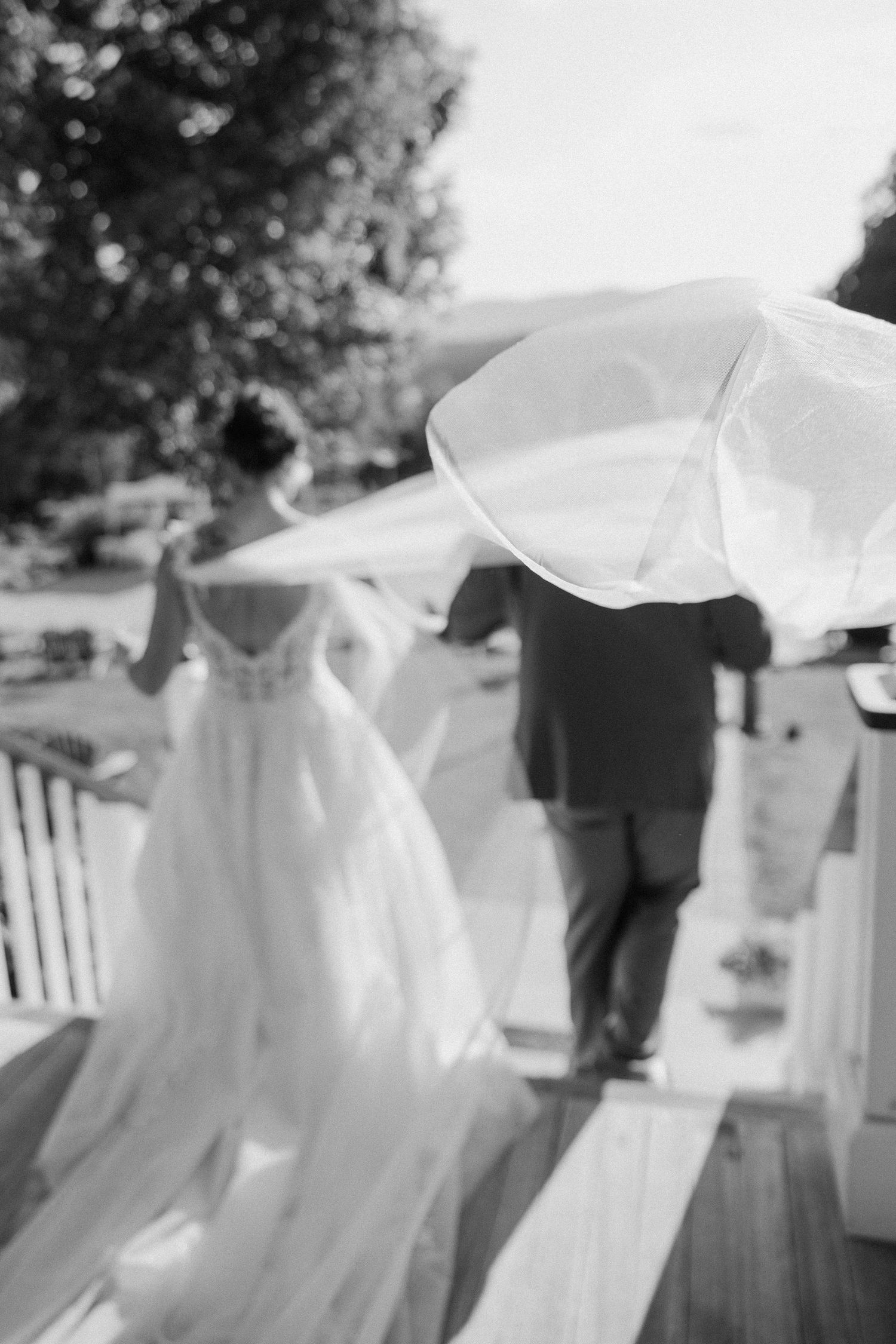 Black and white image of a flowing wedding dress and veil on an outdoor deck.