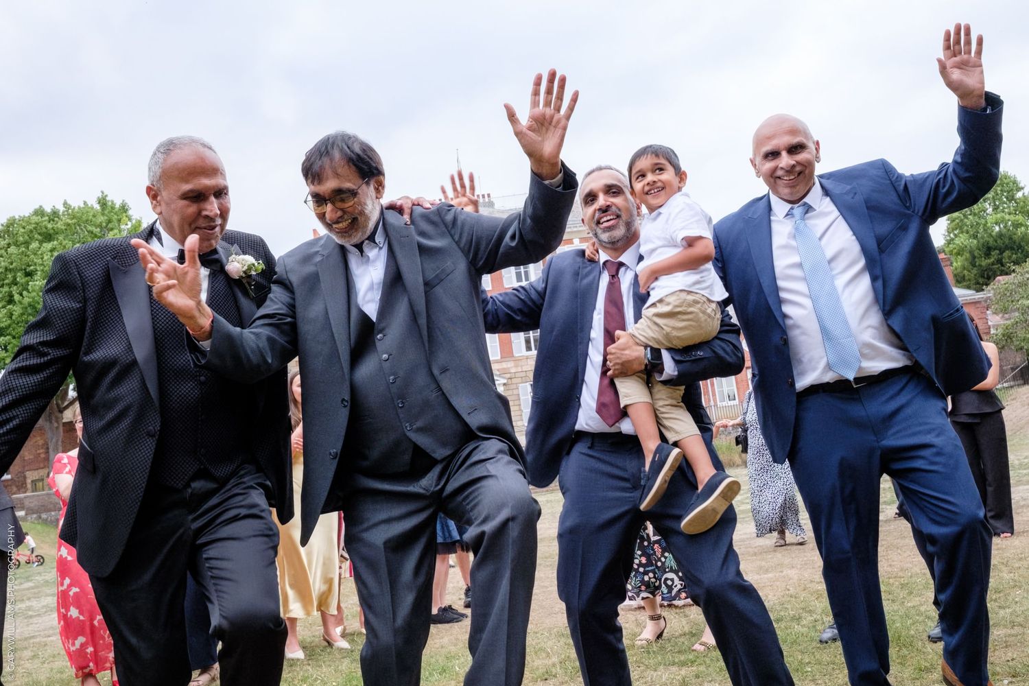 Fun wedding photo of groomsmen leaning to the side in coordinated poses on a sunny outdoor day.