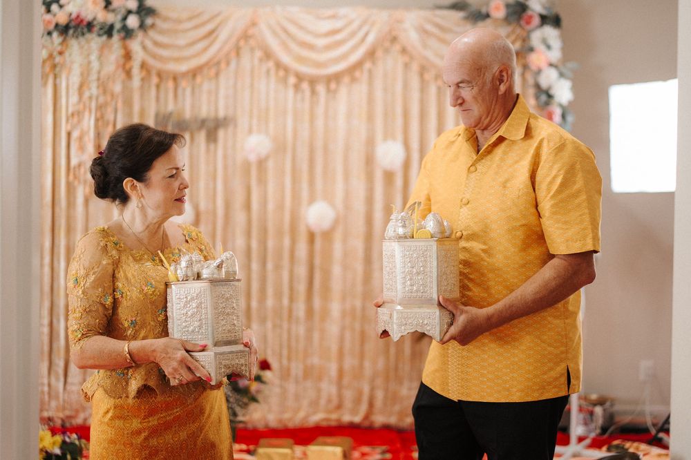 Two people in yellow attire hold white decorative lanterns at an indoor event with elegant drapes in the background.