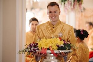 A server in a gold traditional shirt carries a silver tray with colorful flowers at an elegant event.