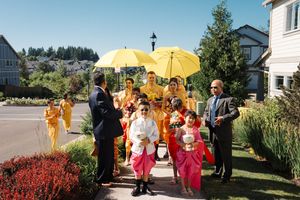 A group gathers under a bright yellow umbrella outside on a sunny day for a special celebration or ceremony.