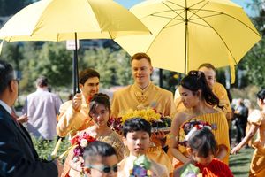 Wedding party members holding yellow umbrellas walk together outdoors during a sunny summer celebration.