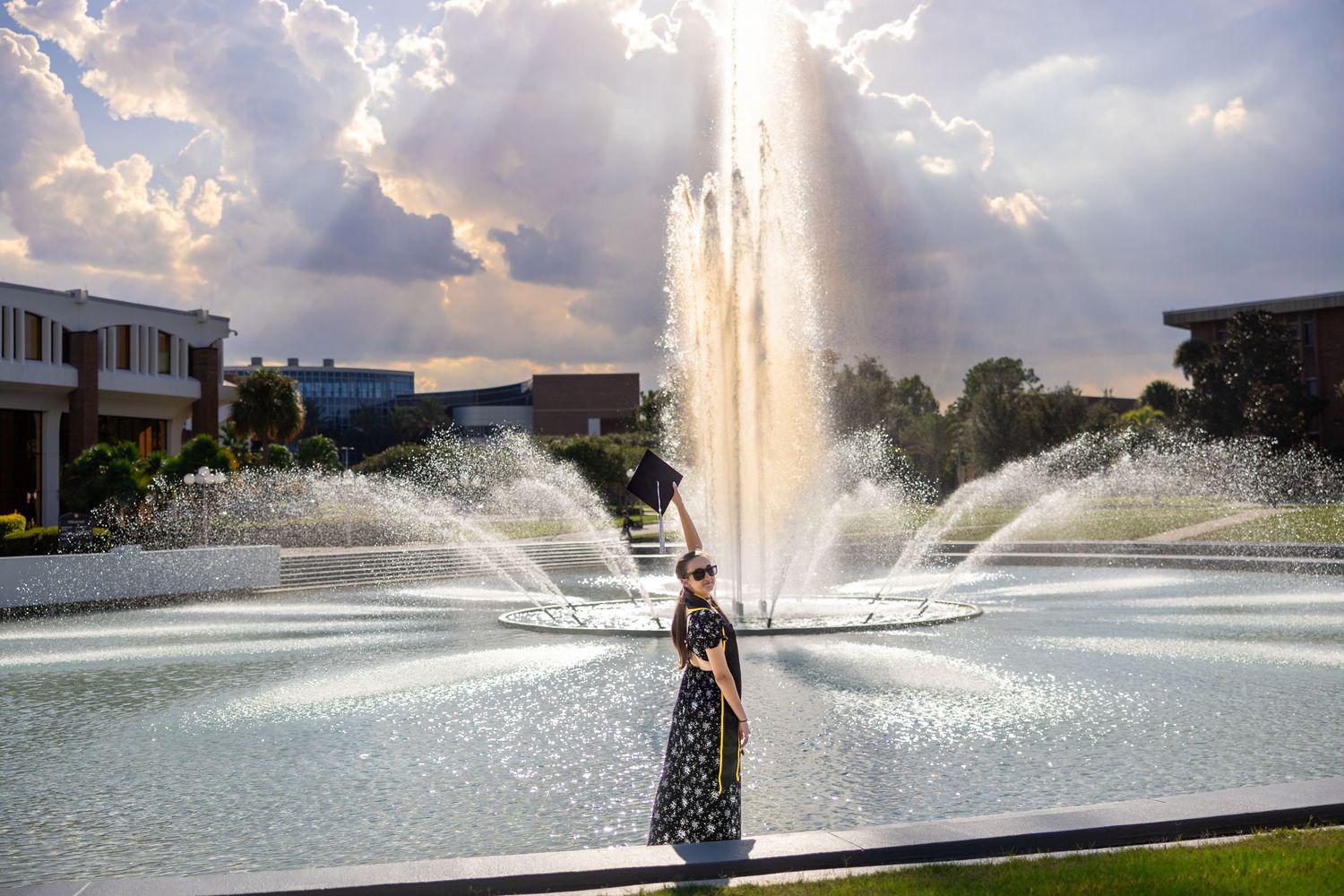 Large fountain spraying water jets in front of modern buildings under cloudy skies.