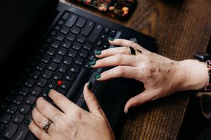 Close-up of hands typing on a black keyboard against a dark wooden desk surface.
