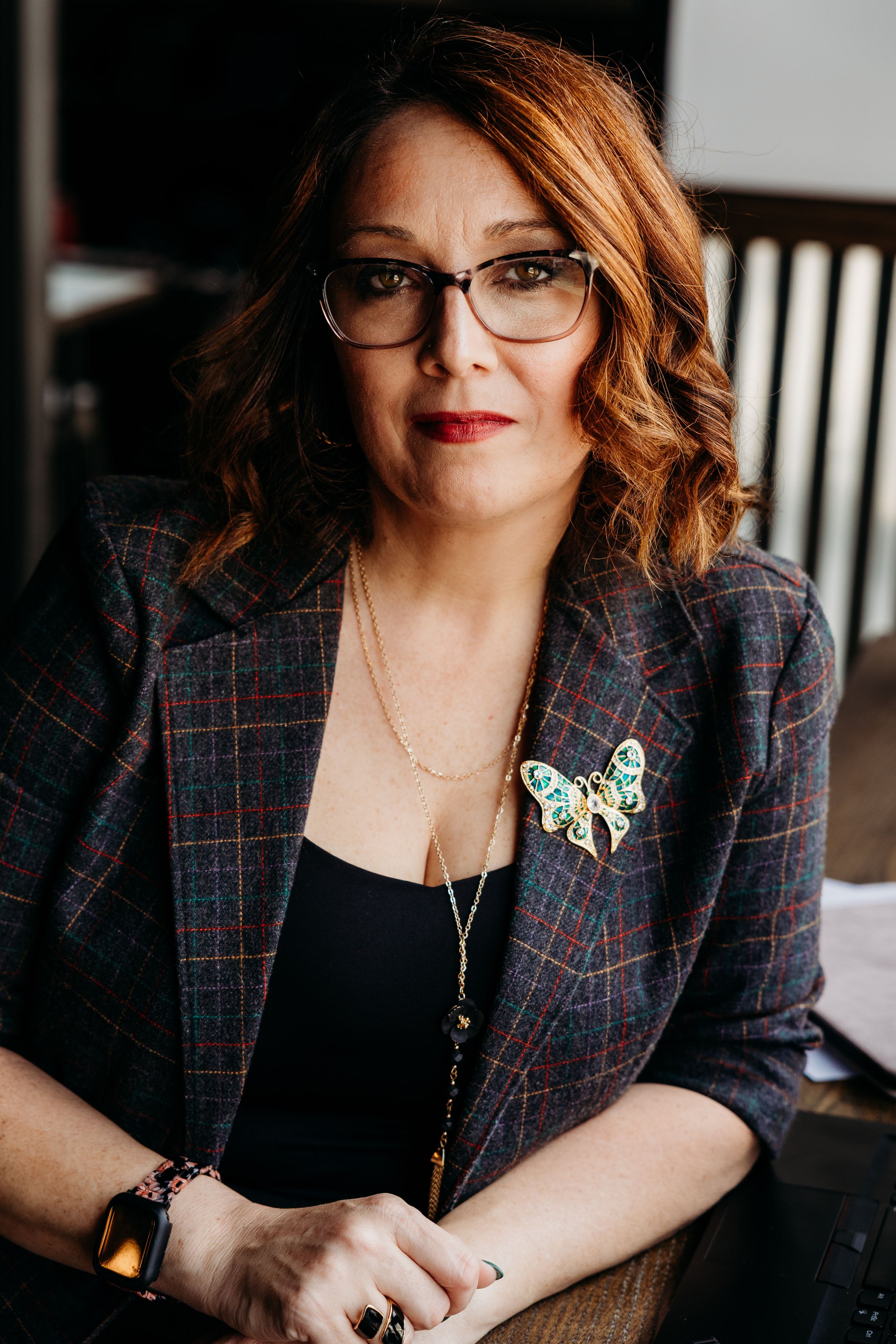 Professional photo series showing a plaid blazer and butterfly brooch accessory in warm indoor lighting.