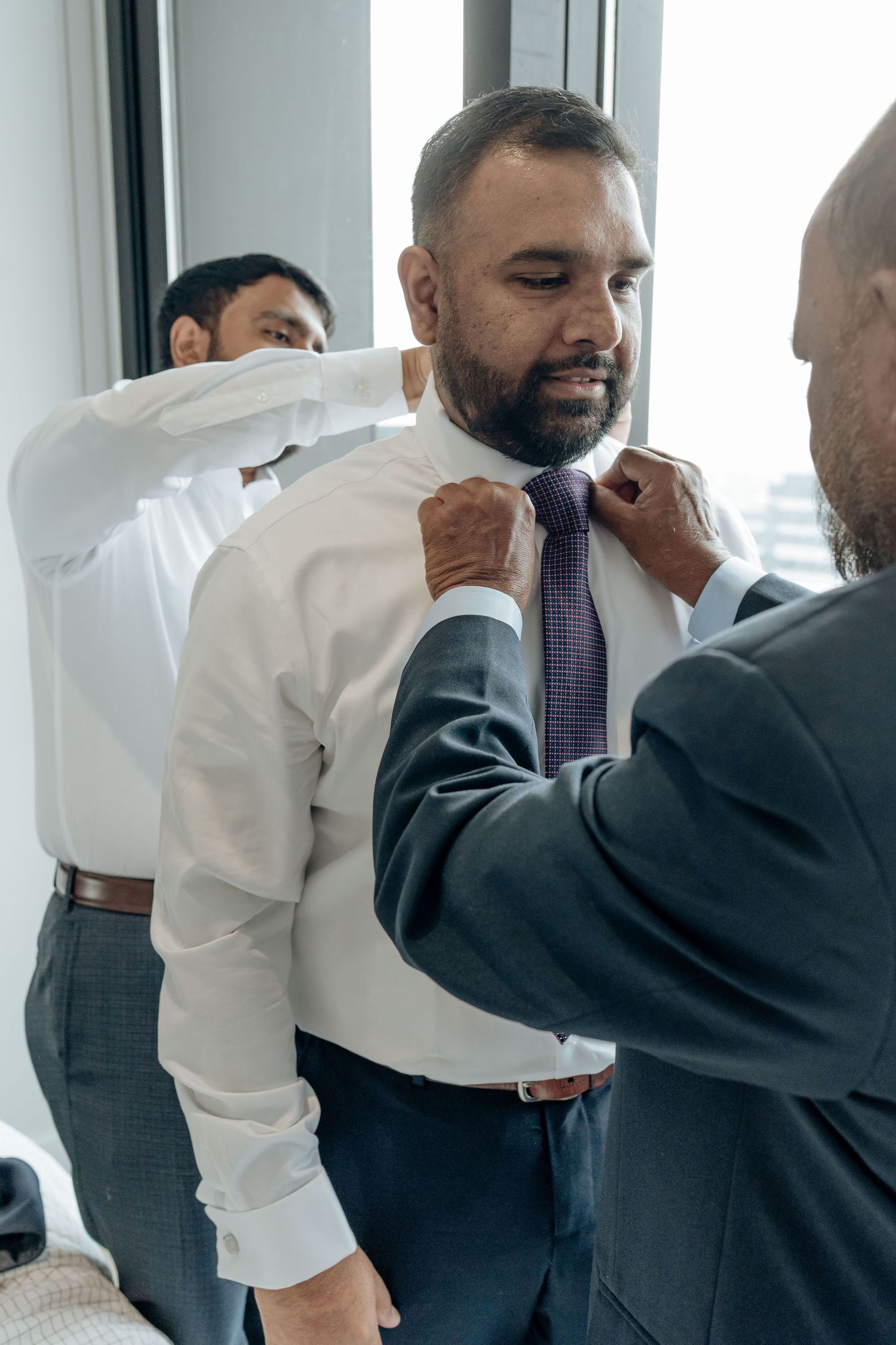 Someone helps adjust a purple necktie on a person wearing a crisp white dress shirt in an office setting.