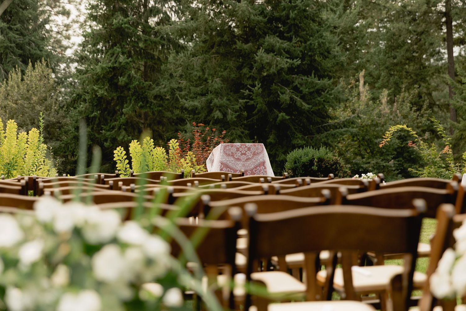Rows of wooden chairs face a floral altar table set for an outdoor garden wedding ceremony.