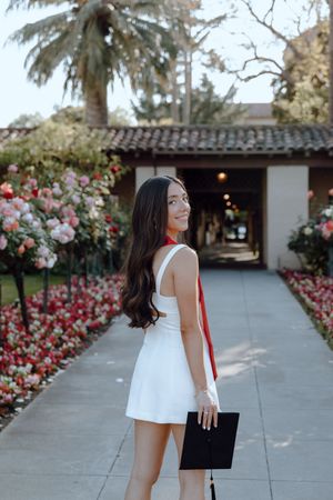 College grad holds her cap in one hand and looks over her shoulder at Santa Clara University. Taken by Bay Area Grad Photographer.
