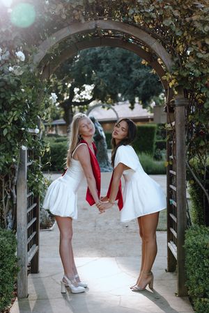 Two college graduates stand apart and fake kiss under an archway at Santa Clara University. Taken by Bay Area Grad Photographer.