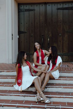 Three college graduates sit on the steps of a church at Santa Clara University together for their grad. Taken by Bay Area Grad Photographer.
