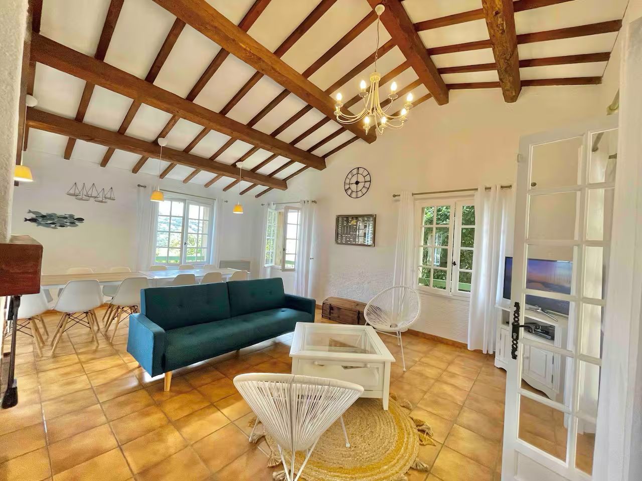 Bright living room with exposed wooden beams, teal sofa, herringbone floors and white rattan furniture in modern style.