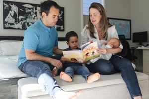 A family sits together on a couch reading a children's book in their living room.