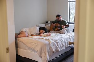 Person sleeping in bed with white bedding while sunlight streams through window.