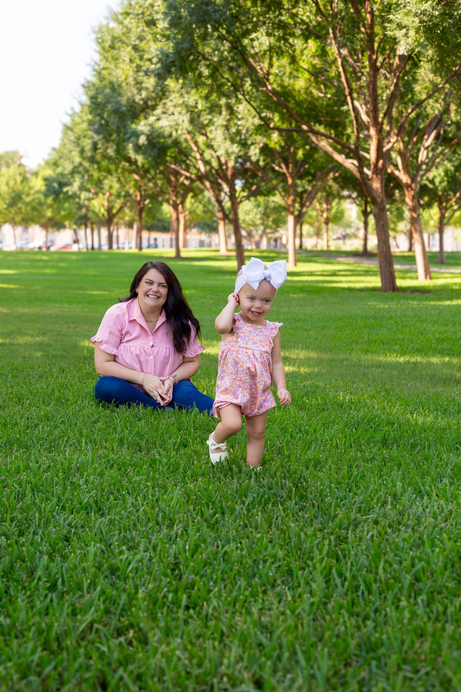 A pair enjoying a playful moment together on lush green grass in a park with trees in the background.