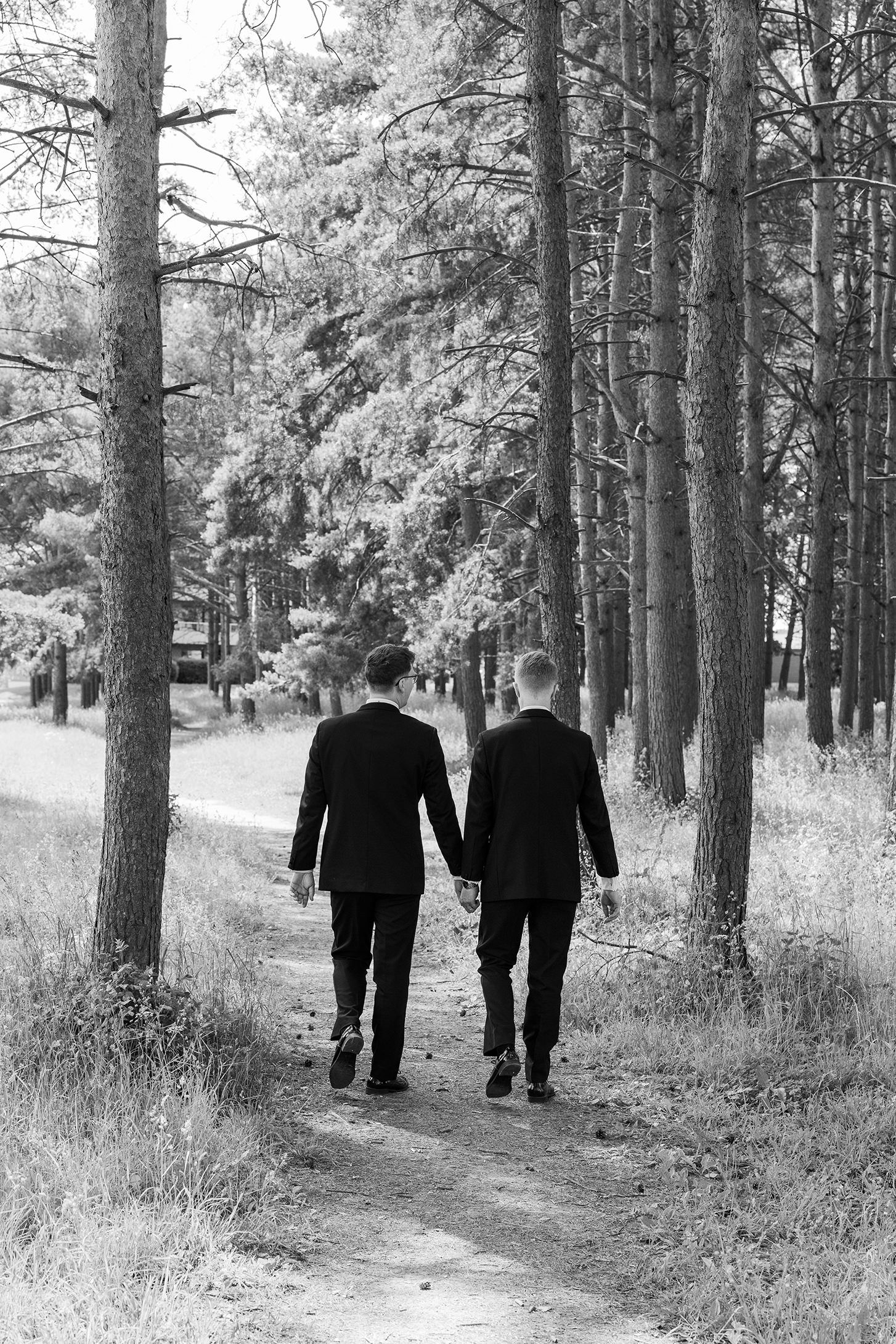 Brudepar hånd i hånd vandrende i skogen. Ser ryggene deres, men det er høye trestammer rundt dem.