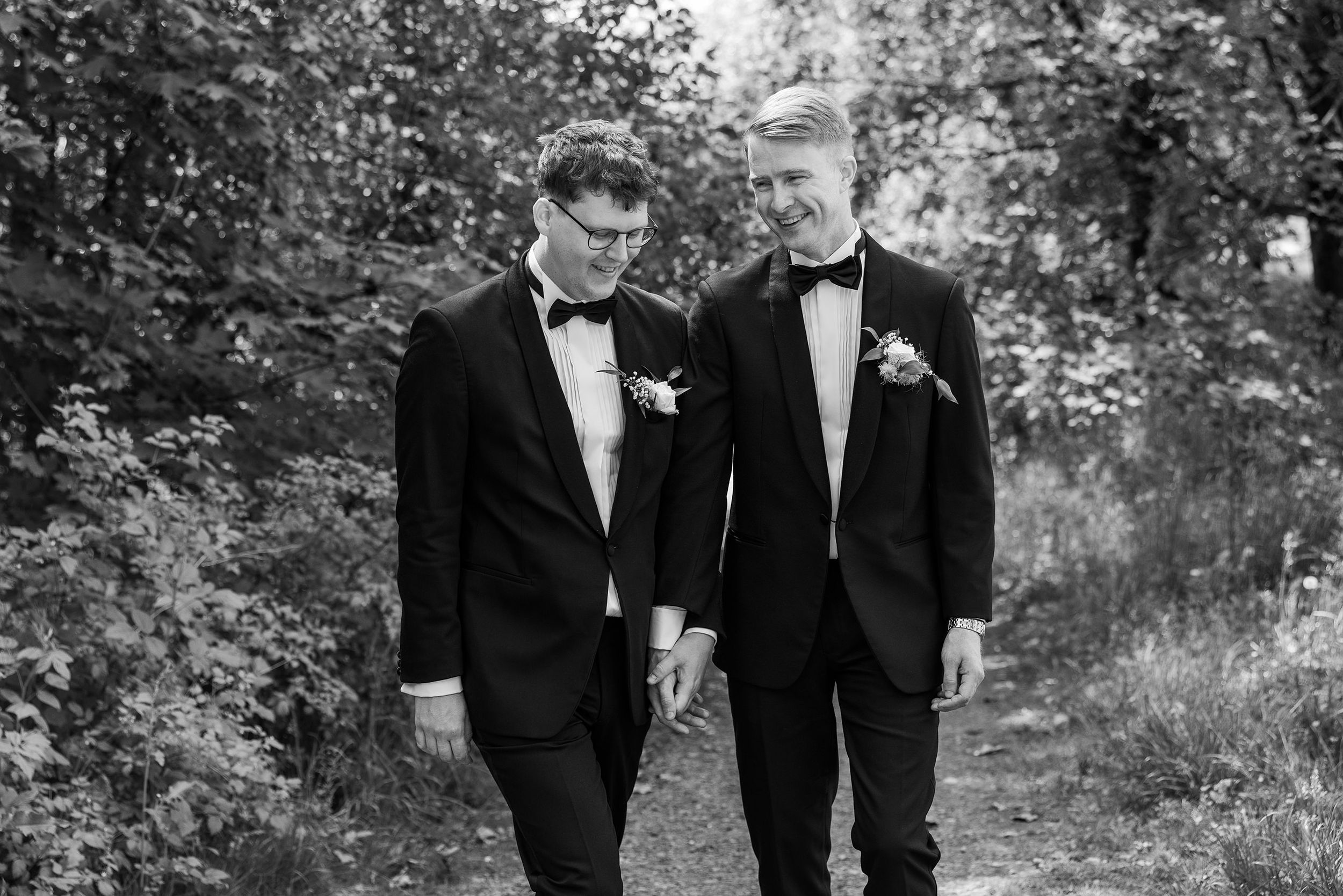Sort-hvitt bilde av brudepar som leier hender og går i en park.
