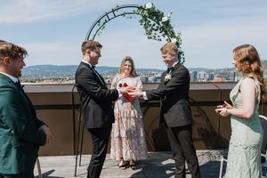 Brudepar som gir hverandre ringer. Vielsen er på en takterrasse med blomsterbue og utsikt over Oslo.