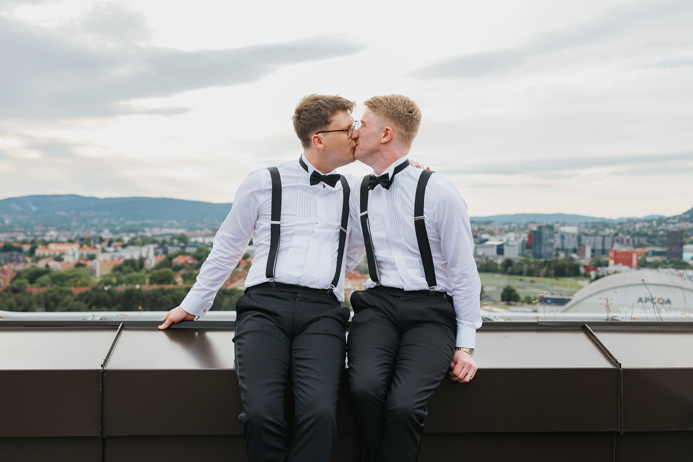 Brudeparet sitter på takkanten og kysser med utsikt over Oslo.