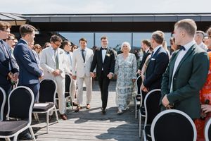 Brudgom går med far og mor i vær sin hånd oppover midtgangen til vielsen på en takterrasse.