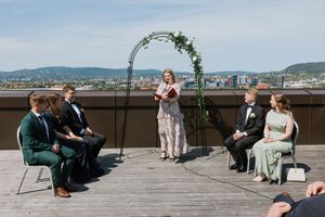 Vielse på takerrasse. Vi ser vigsler i midten og brudgommene sitter på hver sin side sammen med forloverne.