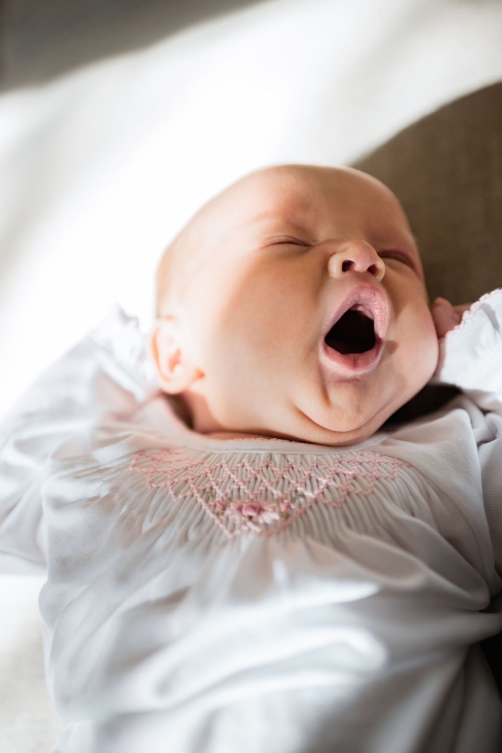A sleeping baby yawns while resting on white bedding in a series of sequential photos.
