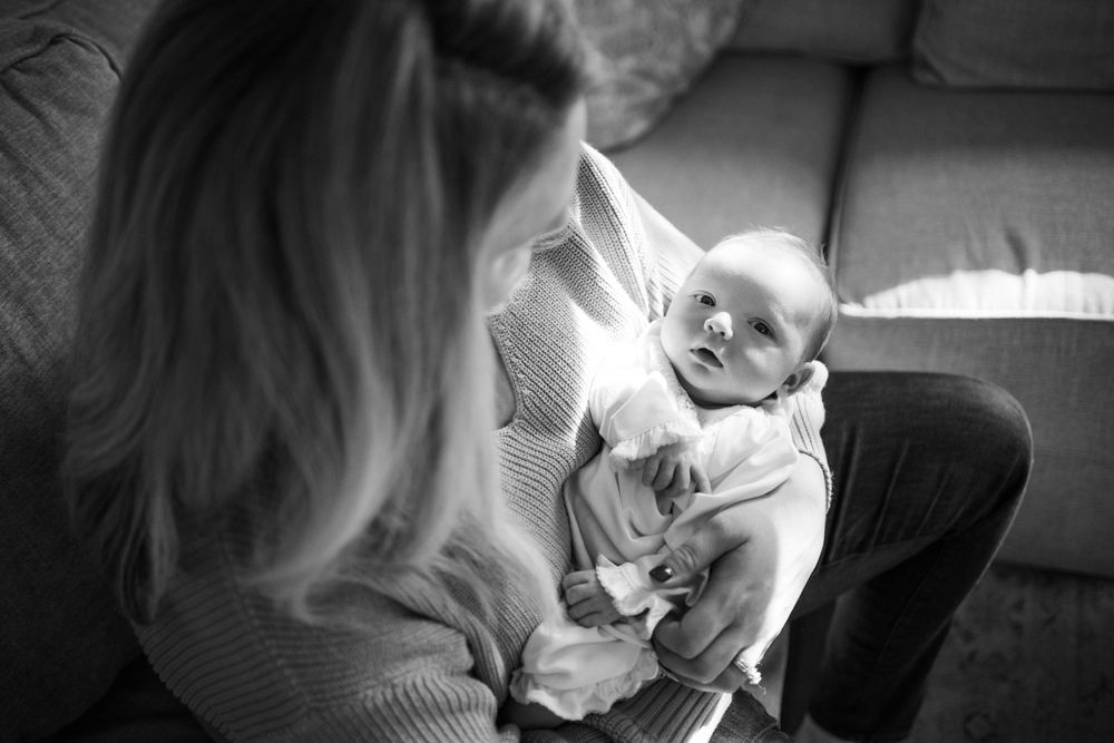 A series of black and white photos showing tender moments between a parent and baby in intimate indoor settings.