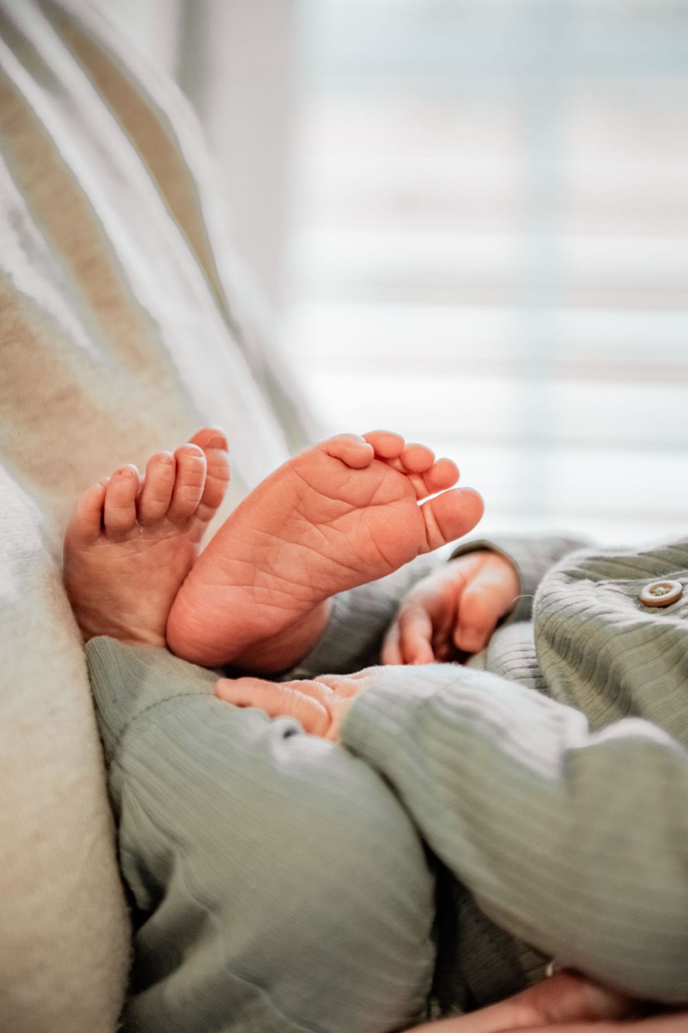 Tiny newborn baby feet peek out from soft green blankets in a peaceful sleeping pose.