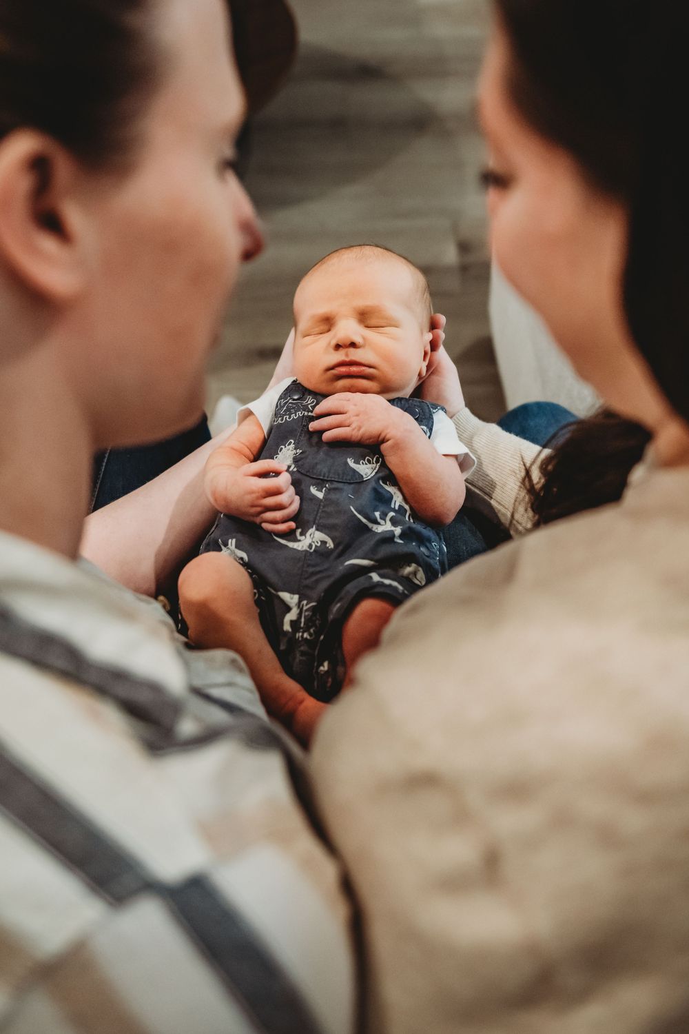 A sleeping baby wearing a navy blue outfit is cradled in someone's arms during an intimate family moment.