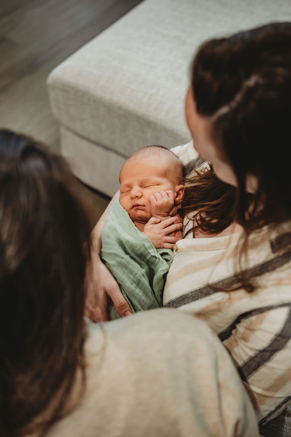 A sleeping newborn baby wrapped in a mint green blanket is cradled lovingly while being admired.