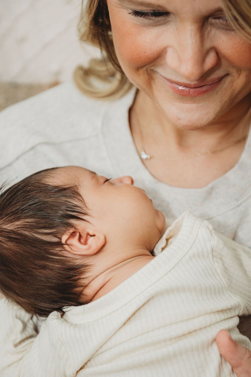 A tender moment between parent and newborn baby in matching white sweaters against a light background.