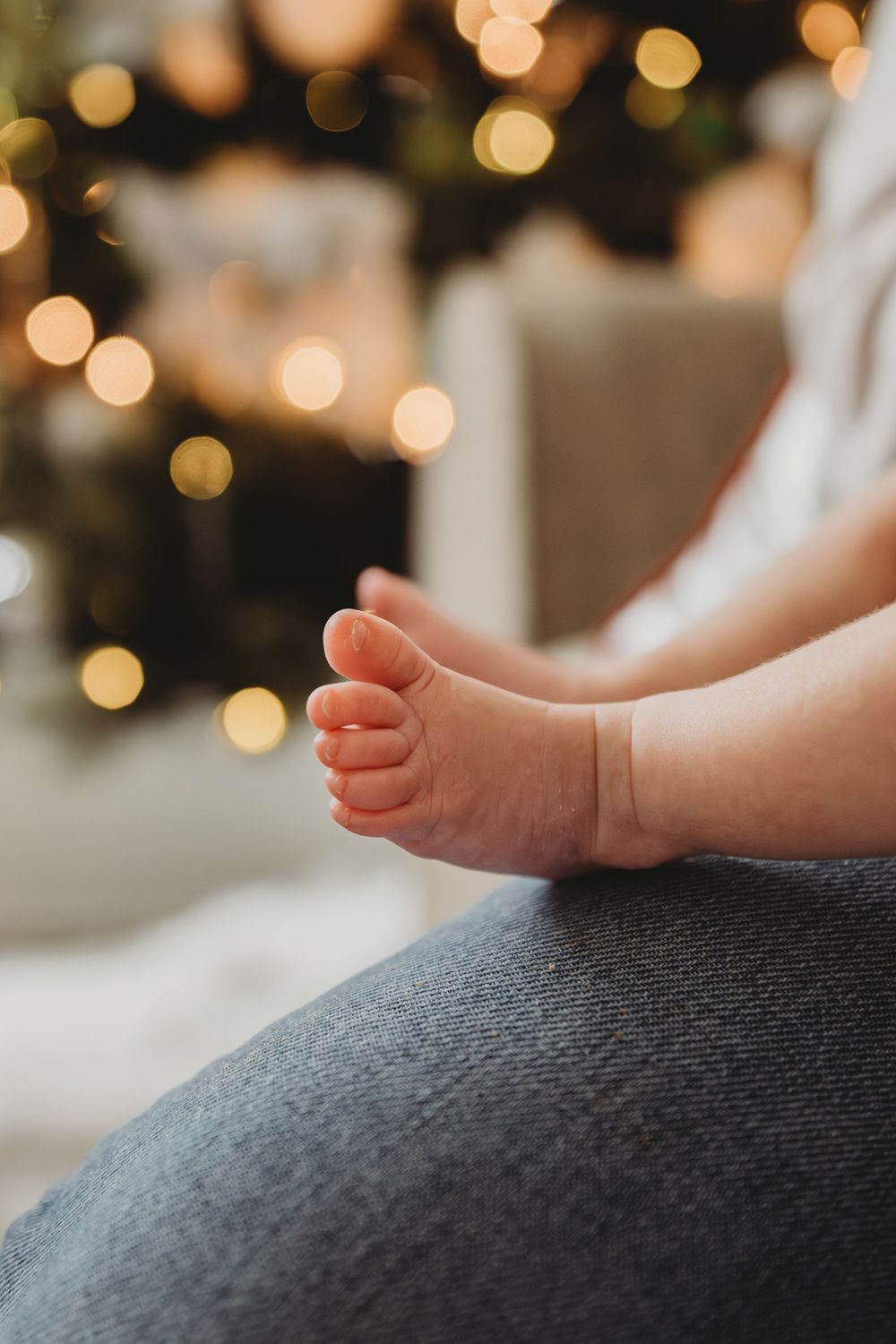 Small baby feet rest on a dark gray surface with soft bokeh lights glowing in the background.