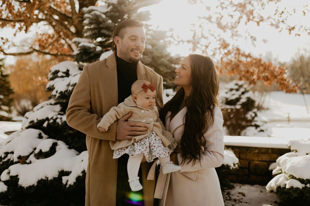 A couple embraces in a romantic autumn setting with warm fall foliage and snow covered ground.