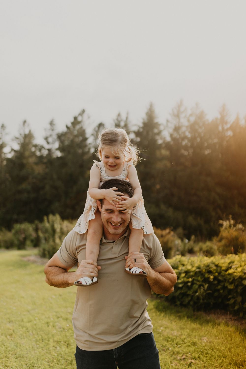A playful moment captured at sunset as someone carries a child on their shoulders in a grassy field.
