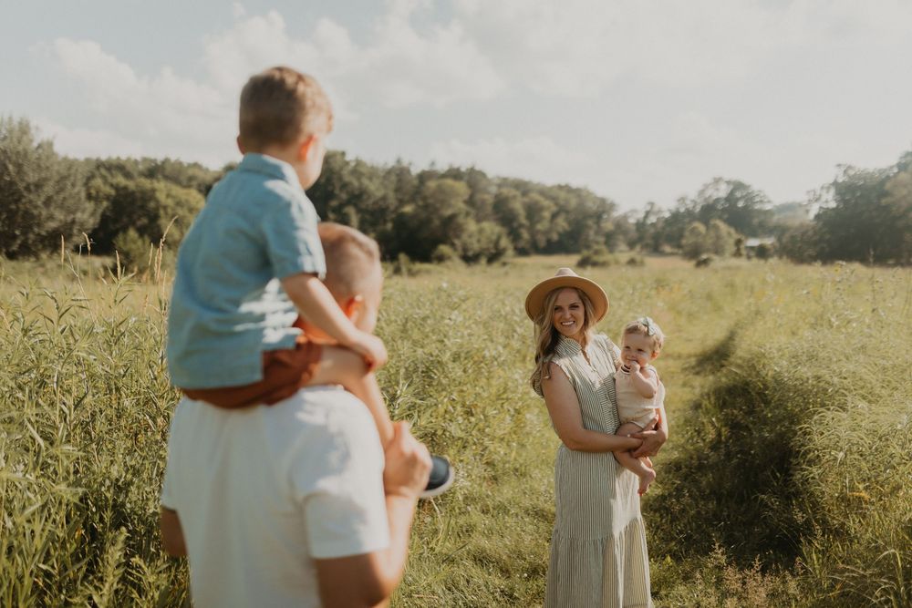 Romantic couple embraces in a sunlit meadow surrounded by lush greenery and wildflowers on a summer afternoon.