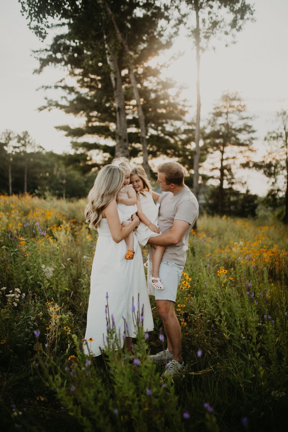 A family shares tender moments together in a field of blooming wildflowers during golden hour.