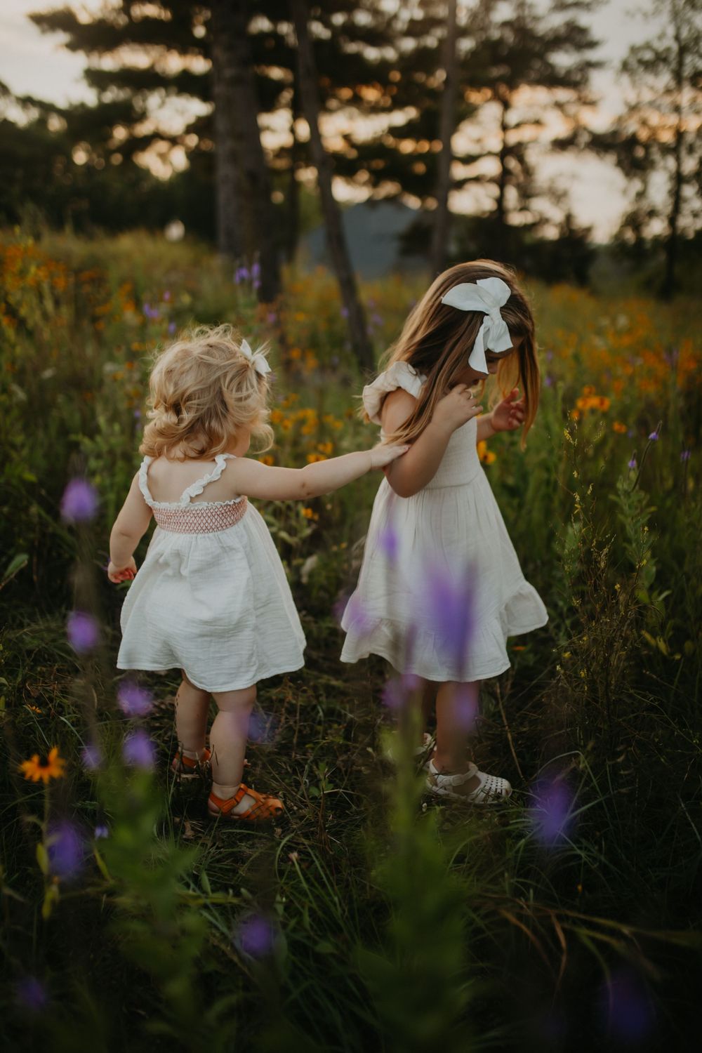 Children playing together among purple and yellow wildflowers in a summer meadow at golden hour.