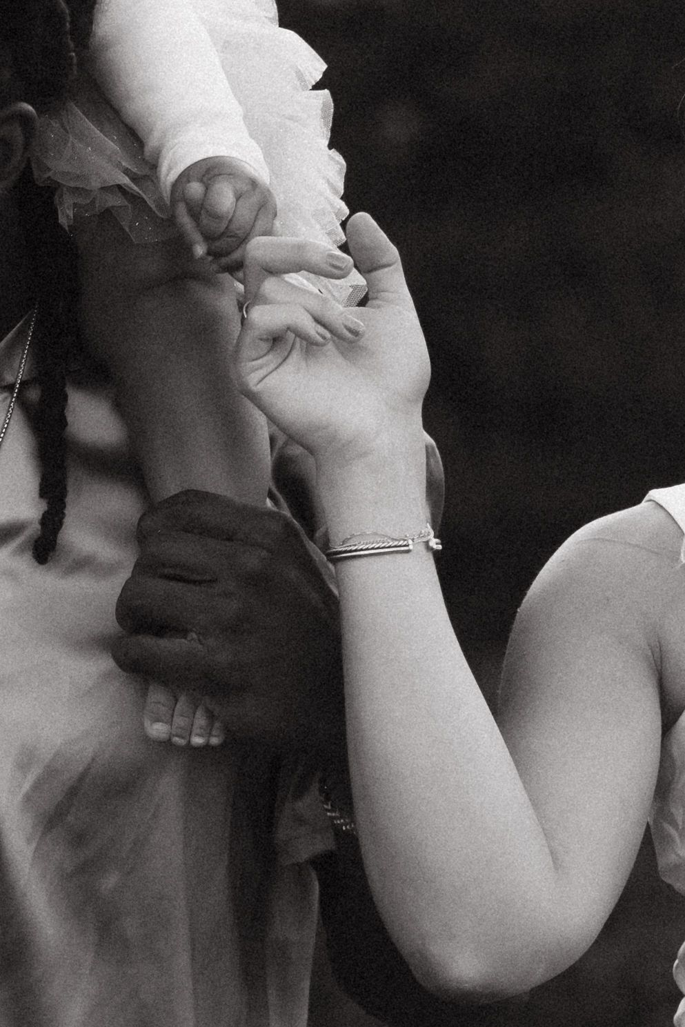 Black and white close-up of hands clasped together showing a bracelet and contrasting skin tones in an intimate moment.