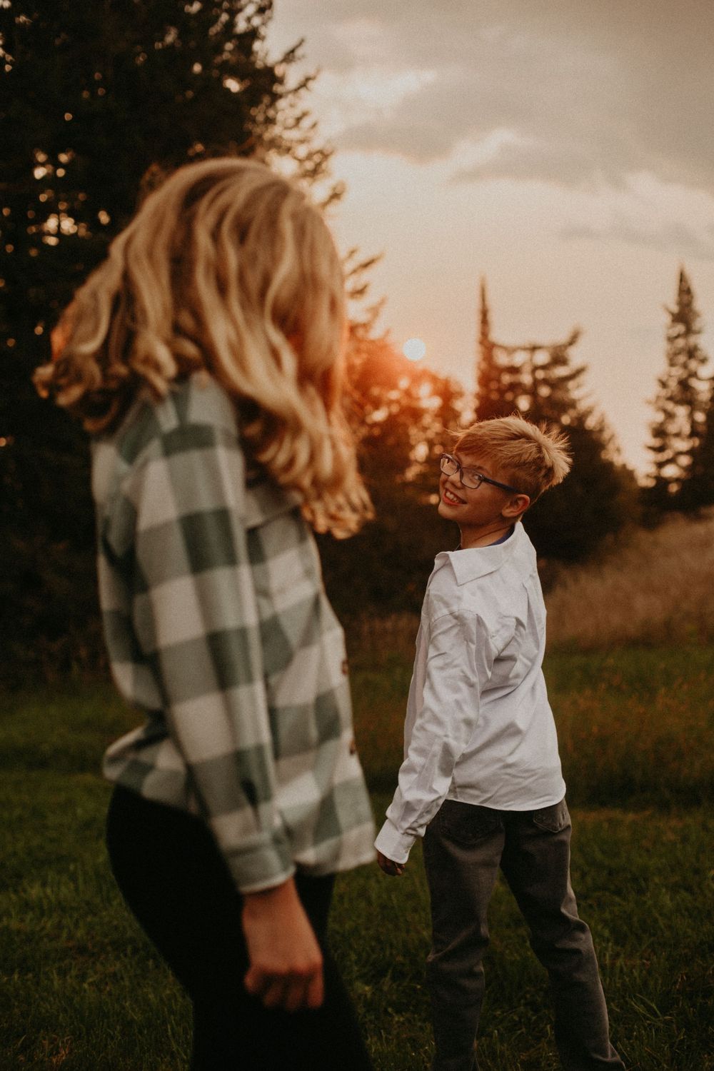 Two people dancing playfully in a grassy field at sunset wearing plaid and white clothing.