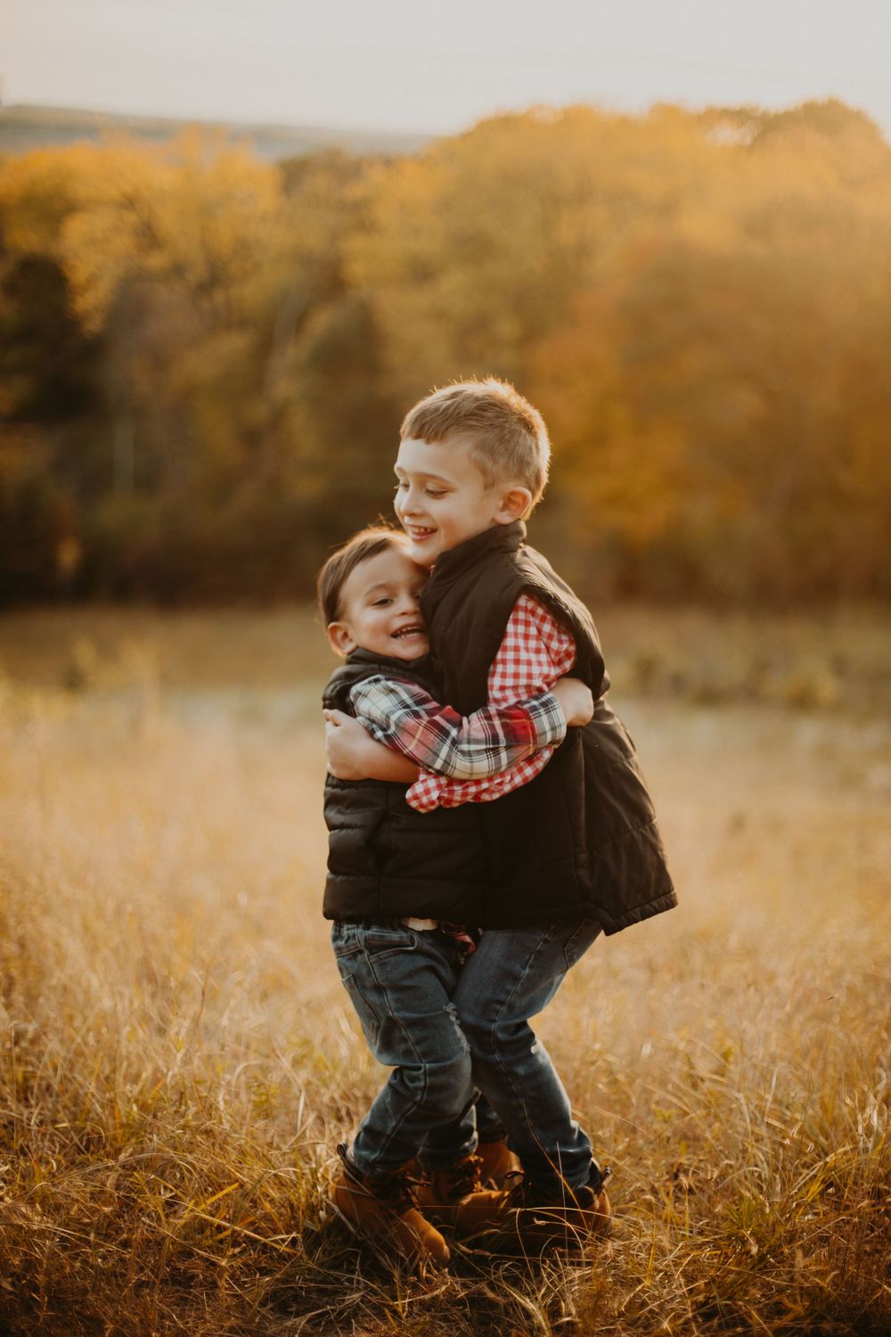 Two children hug and play together in a golden autumn field at sunset.