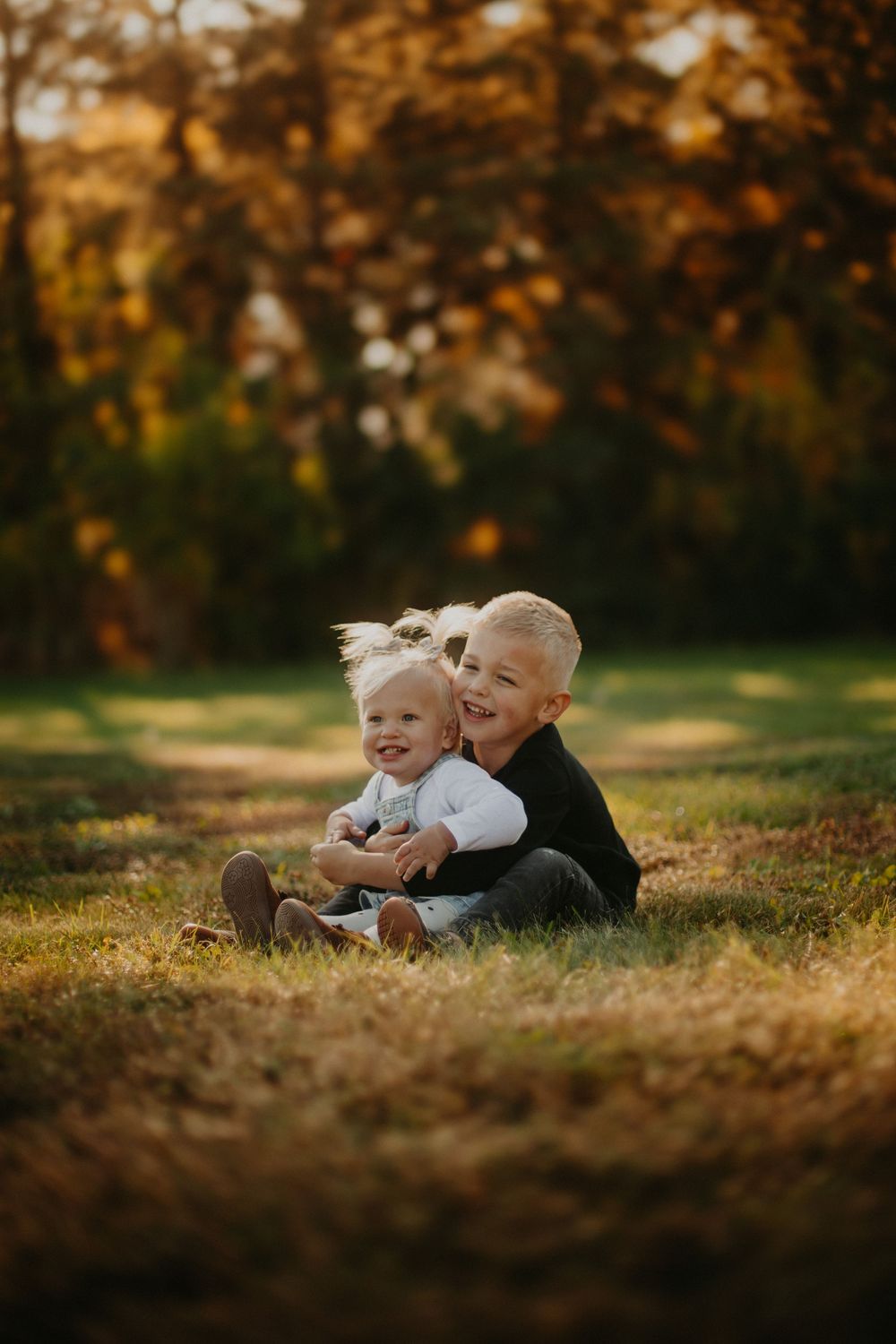 Two children lying together on autumn grass during golden hour sunset photography session.