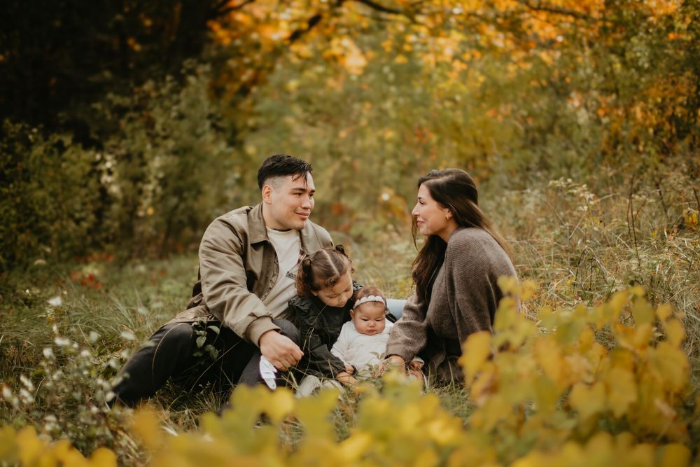 A family enjoys a warm autumn day together in a park surrounded by golden yellow foliage.