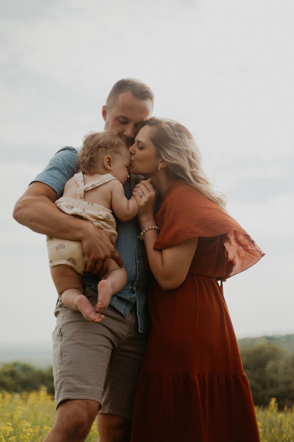 A tender family moment captured in a field of yellow wildflowers against an overcast sky.